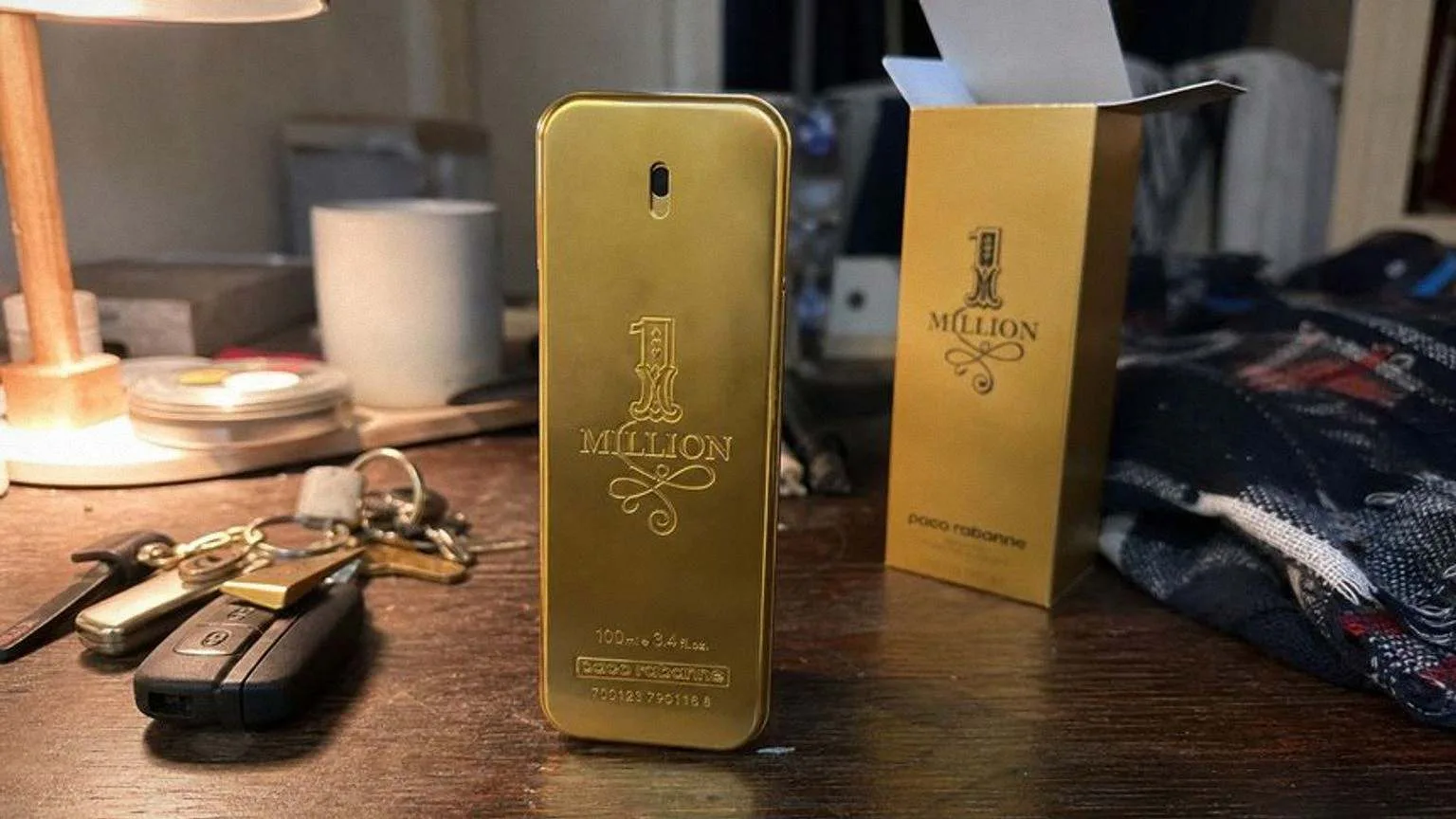 The gold 1 Million bottle beside its open carton on a dark wood dresser, next to car keys and a folded checked scarf